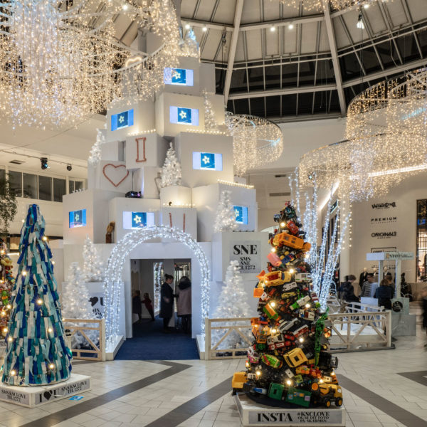 Trees made of old teddy bears, toy cars and socks in front of a light arch leading into a giant christmas tree made of white boxes inside the shopping center Kolding Storecenter in the city of Kolding, Denmark.
