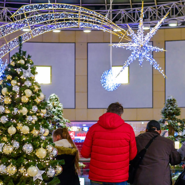 Light greenery trees with golden and silver baubles and light motifs of shooting stars and snow crystalls hanging from the ceiling inside a shopping center.
