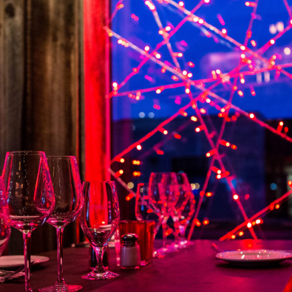 Glases on a table in front of with red light strands decorated windows of the restaurant Rouge Boeuf in the city of Montréal, Canada.